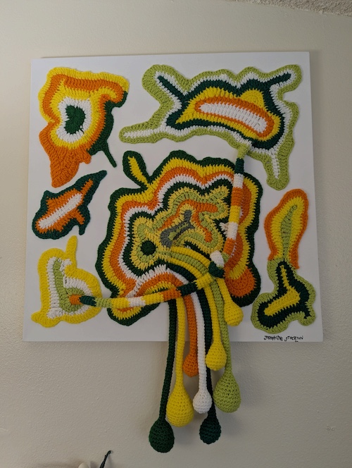 An abstract freeform fiber tapestry in green, orange, yellow, and black