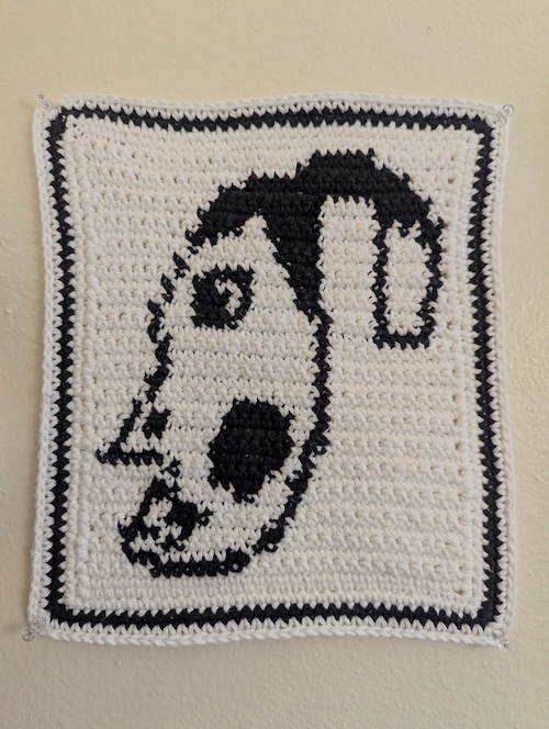 A black and cream crocheted tapestry showing an expressive face