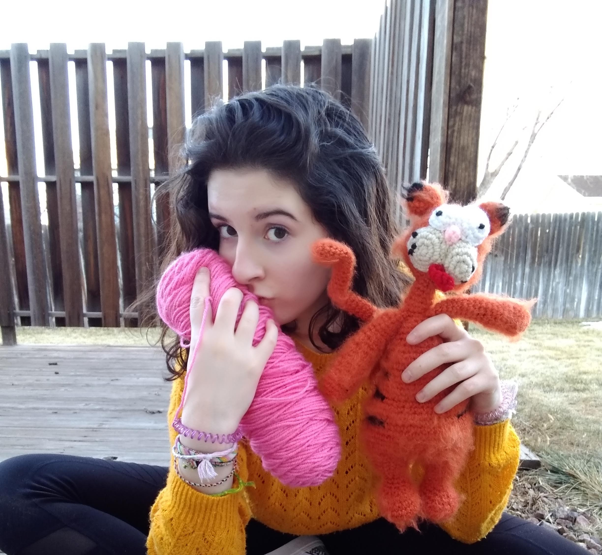 Joey kissing a pink skein of yarn while holding a crocheted cat