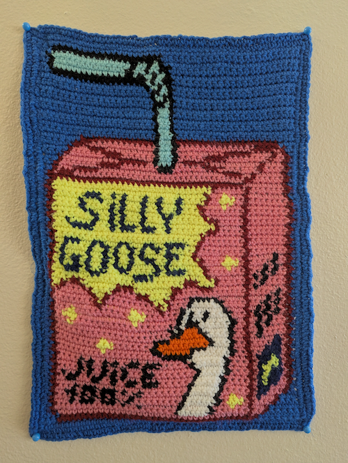 A colorful crocheted tapestry depicting a pink juice box labeled Silly Goose Juice with a goose on the front
